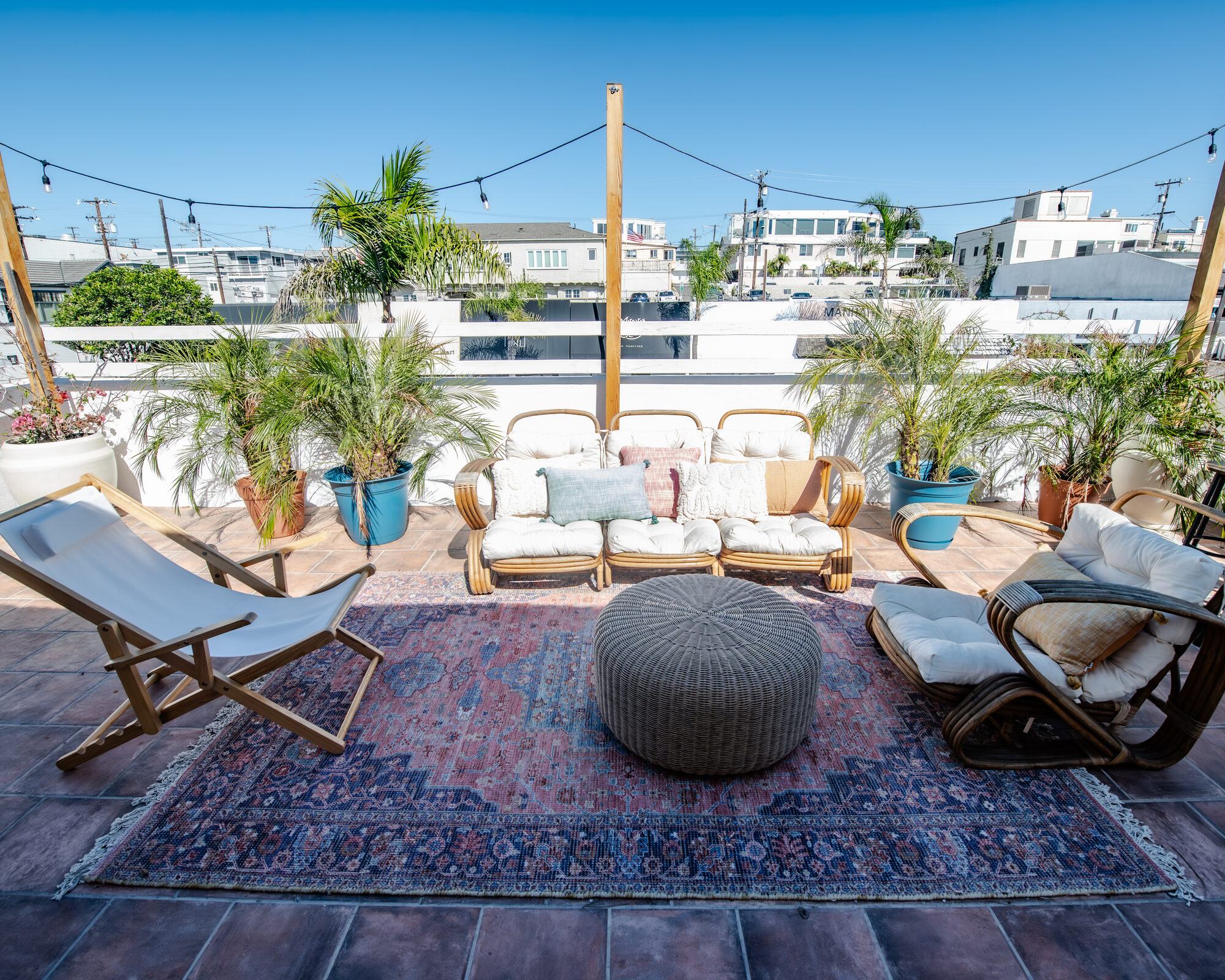 Boho-luxe rooftop patio at Tropical Refuge — rattan seating, vintage rug, palms and string lights in Manhattan Beach