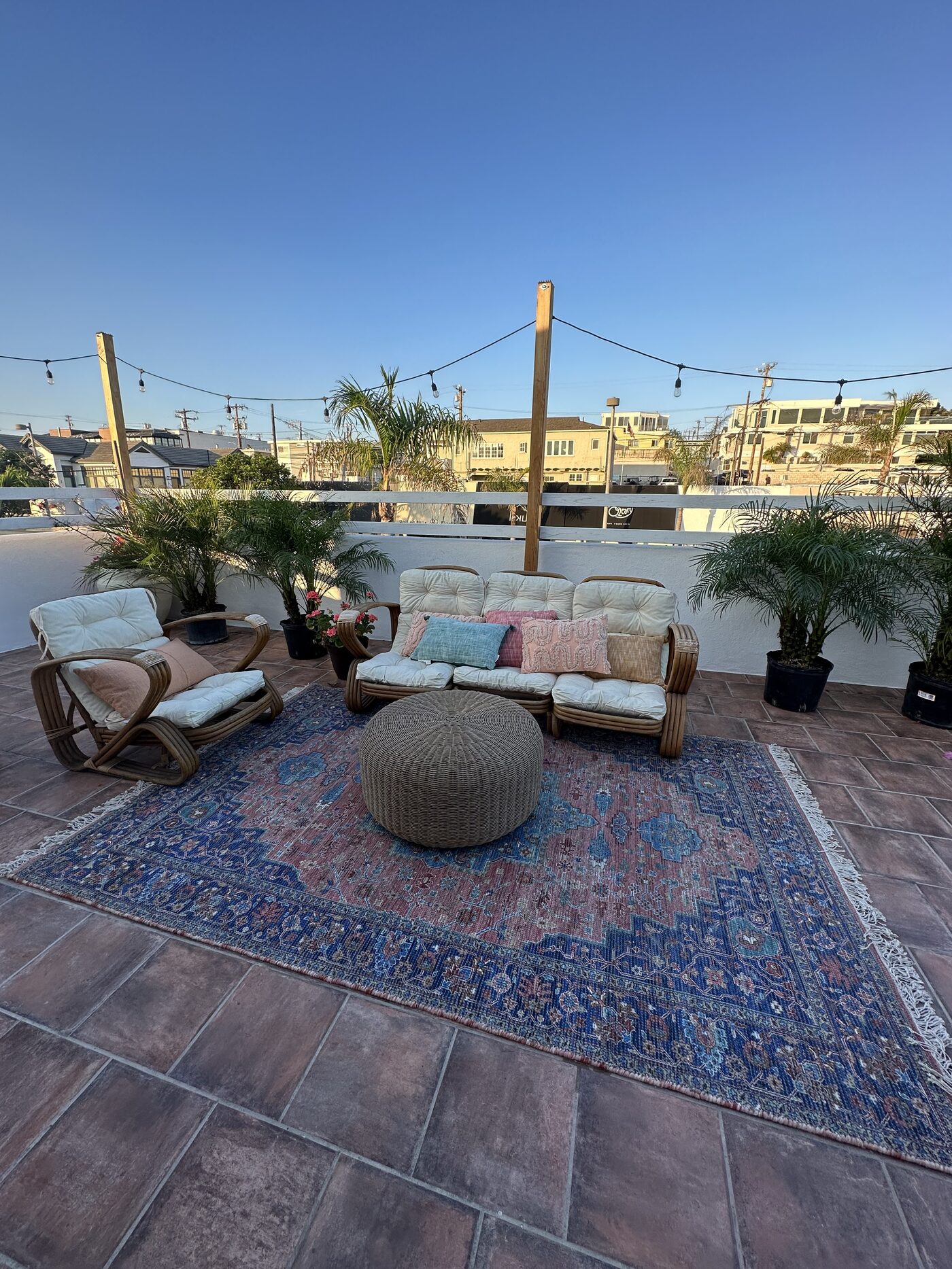 Rooftop patio at golden hour with ocean-view fence, palms and string lights